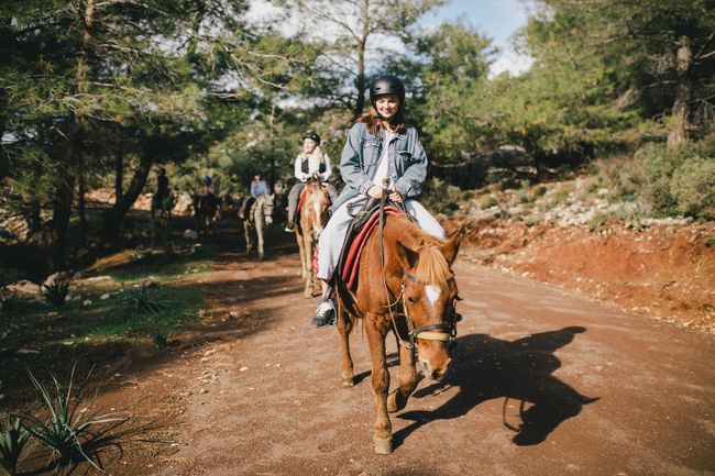Group of people wearing riding helmets walking on horseback through picturesque places.