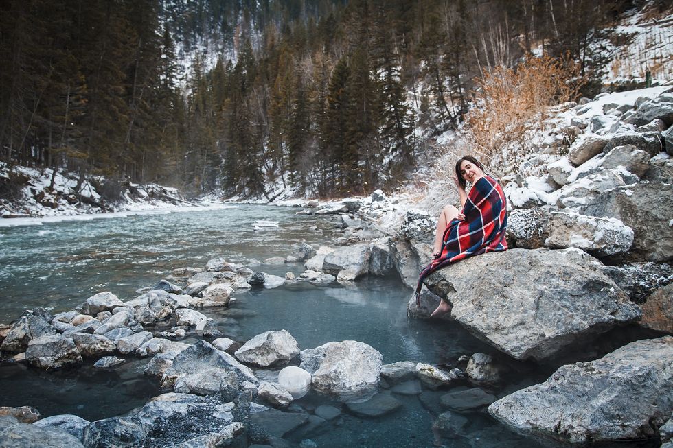 Young female traveler relaxing at natural hot springs during winter time in Lussier, BC, Canada. Pools with hot water right next to cold freezing river. Winter activities, getaway, hideout.