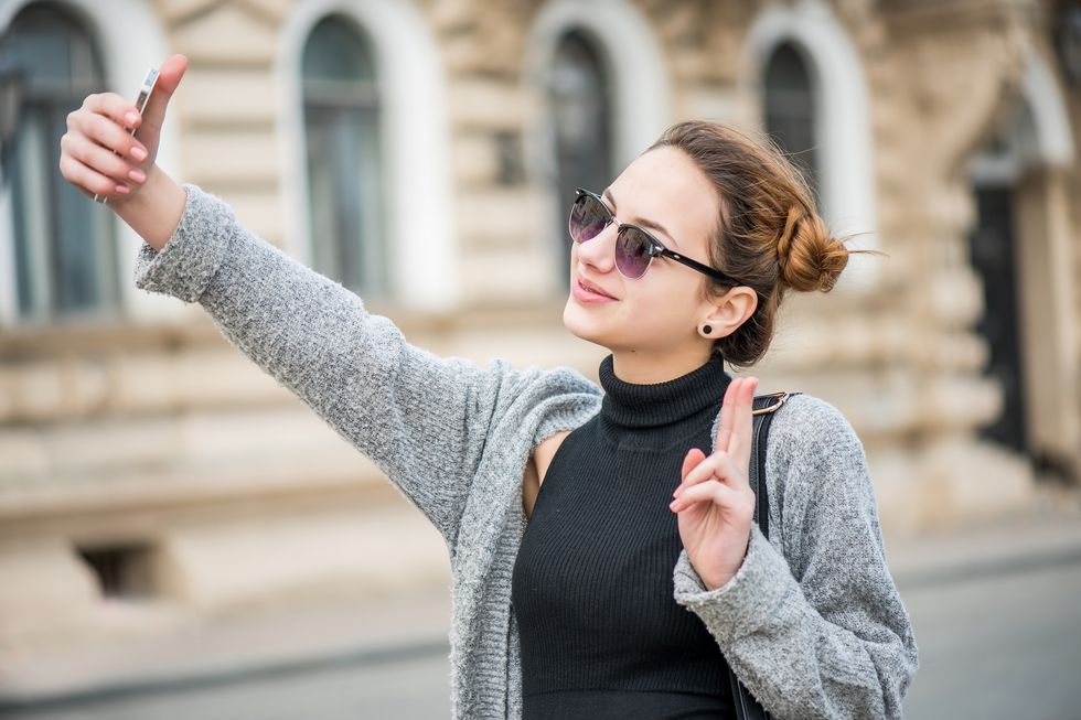 Female standing taking selfie holding up the peace sign.