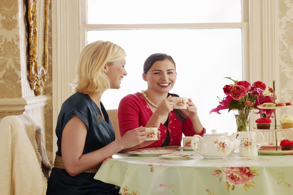 Portrait of two smiling young women having tea at dining table