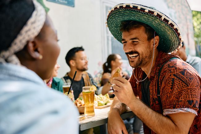 Happy man eating nacho ships with guacamole while being with his friends in Mexican restaurant.