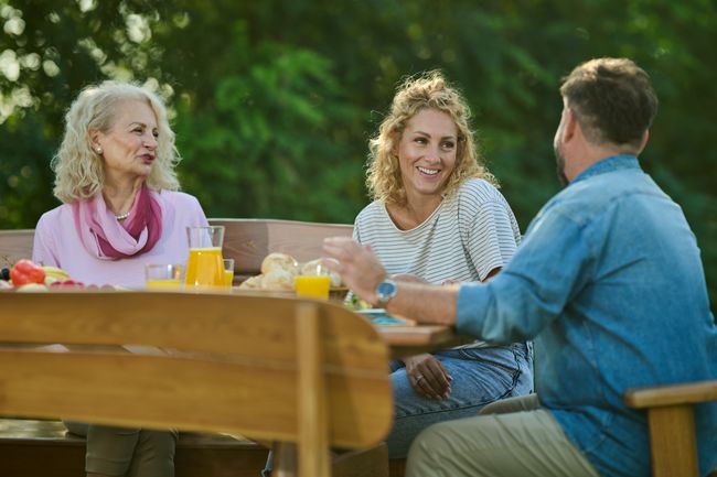 Family is sitting at a picnic table outside, enjoying each other's company over brunch. They are laughing and talking while they eat