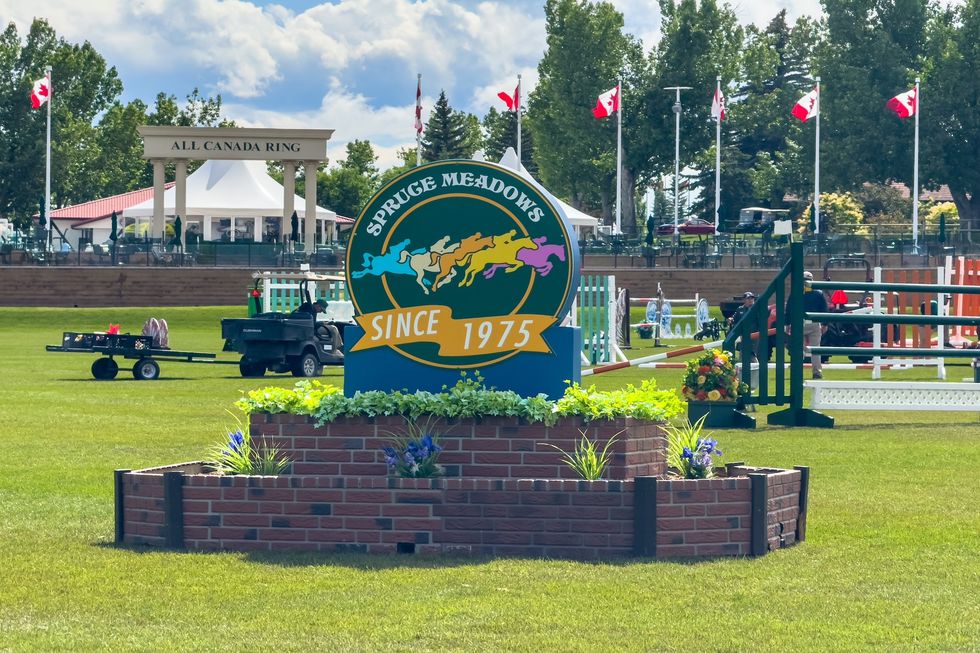A wide shot of Spruce Meadows, a premier equestrian facility in Calgary, Alberta, featuring its iconic sign and verdant show jumping grounds.