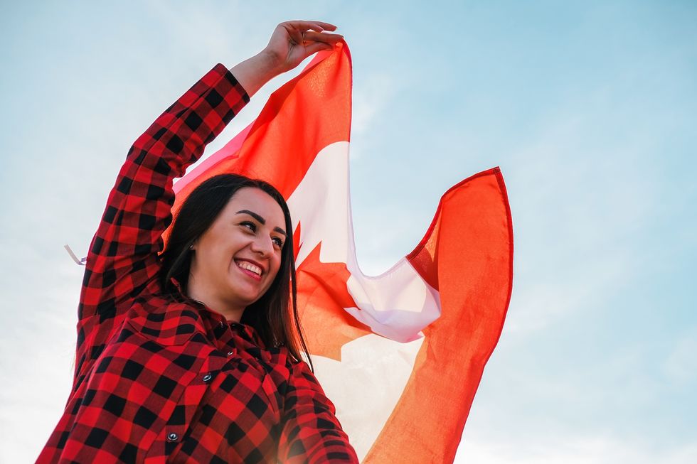 Young millennial brunette woman holding The National Flag of Canada. Canadian Flag or the Maple Leaf. Tourist traveler or patriotism. Immigrant in a free country. Independence day 1th july
