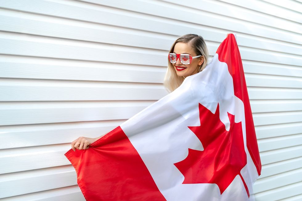 blond hair female person holding national Canadian flag cover her body. Pretty women smiling and holding big Canadian flag and wear sunglasses. Canada Day banner concept.