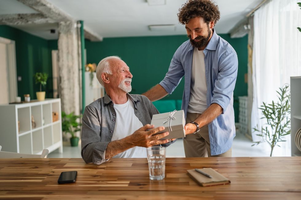 Adult son joyfully giving a thoughtful gift to his senior father at home, capturing the essence of love and care in their family relationship during a special celebration