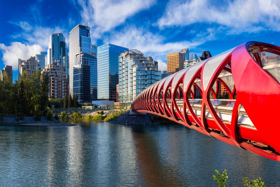 Calgary peace bridge Peace Bridge across Bow River with Modern City Buildings in Background during a vibrant summer sunrise. Taken in Calgary, Alberta, Canada.