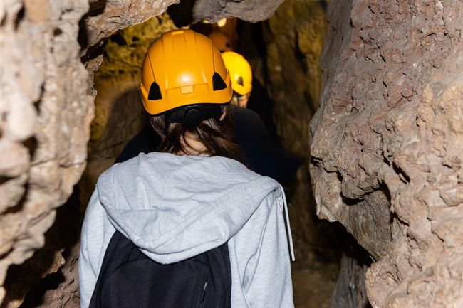 Close-up of people exploring subterranean passages during an extreme guided caving tour, focused on the safety gear.