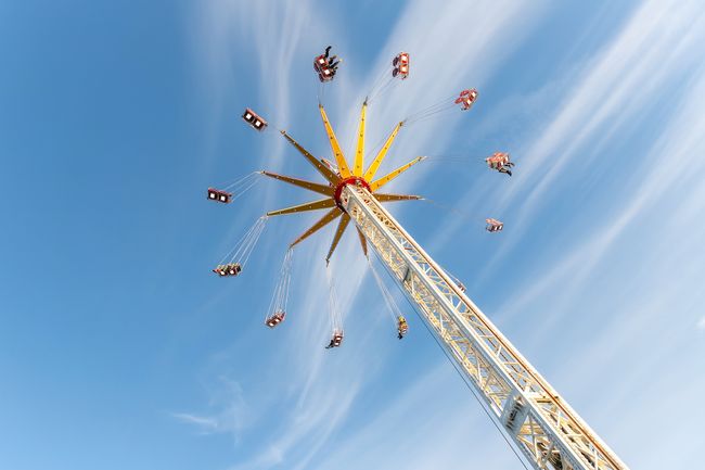 Scenic bottom view high chain swing flying carousel against blue sky. Merry go round roundabout chairoplane at portable amusement park. People enjoy having family fun play riding at fair festival