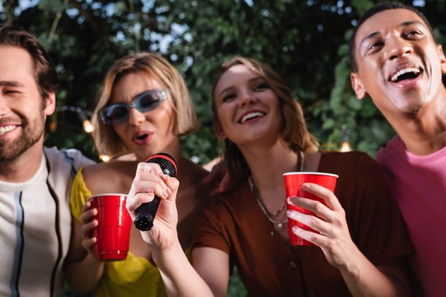 Cheerful friends with plastic cups singing karaoke outdoors