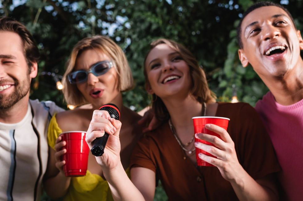 Cheerful friends with plastic cups singing karaoke outdoors