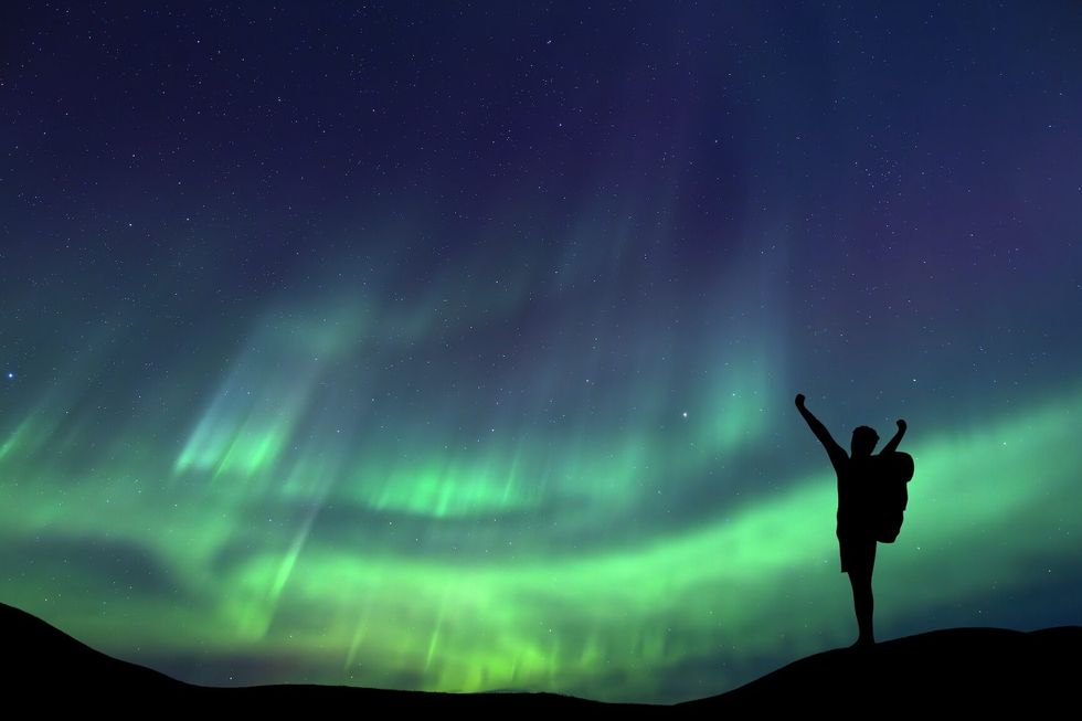 A person is observing a magnificent Aurora Borealis light display in an open field Success concept.