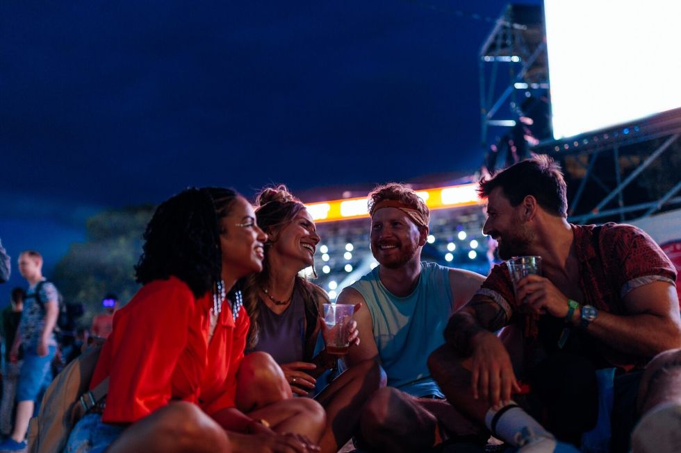 Young people sitting and toasting with beers at a concert in the open air at a music festival.