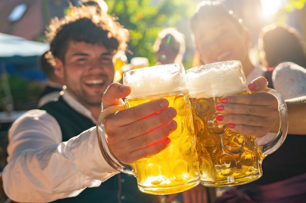 Two people in traditional tracht clinking beer mugs and smiling at sunny day at oktoberfest or beer garden in germany