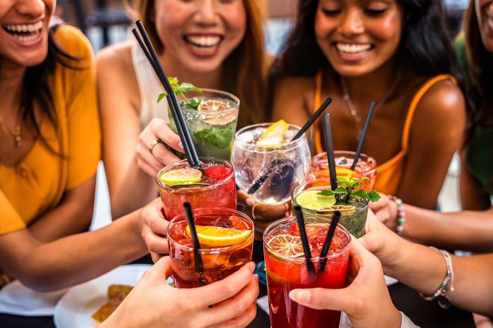 Happy people toasting cocktail glasses sitting at bar table - Cheerful friends enjoying happy hour at pub restaurant balcony - Food and beverage life style concept