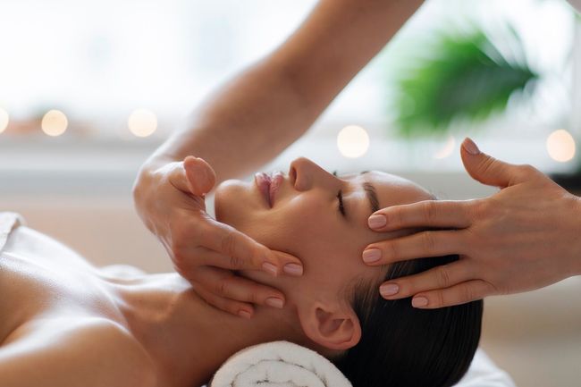 Spa relaxation. Young woman enjoying facial massage, relaxing during face building treatment, side view shot