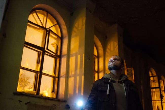 Man with flashlight in dark creepy abandoned mansion at night