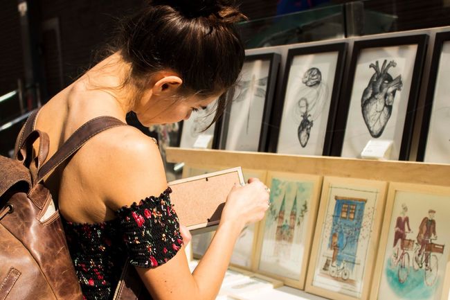 woman choosing a drawing or a painting to buy at a market place.