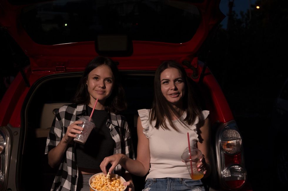 Two female friends with popcorn sitting in the car while watching a movie at drive in cinema. Selective focus. Entertainment, leisure activities, hobby concept