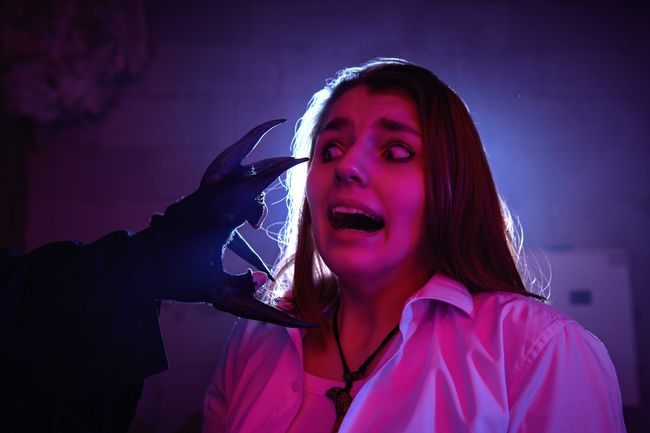 A frightened girl screams in horror when she stumbles upon the hand of a monster with large black claws in a dark basement. Halloween quest.