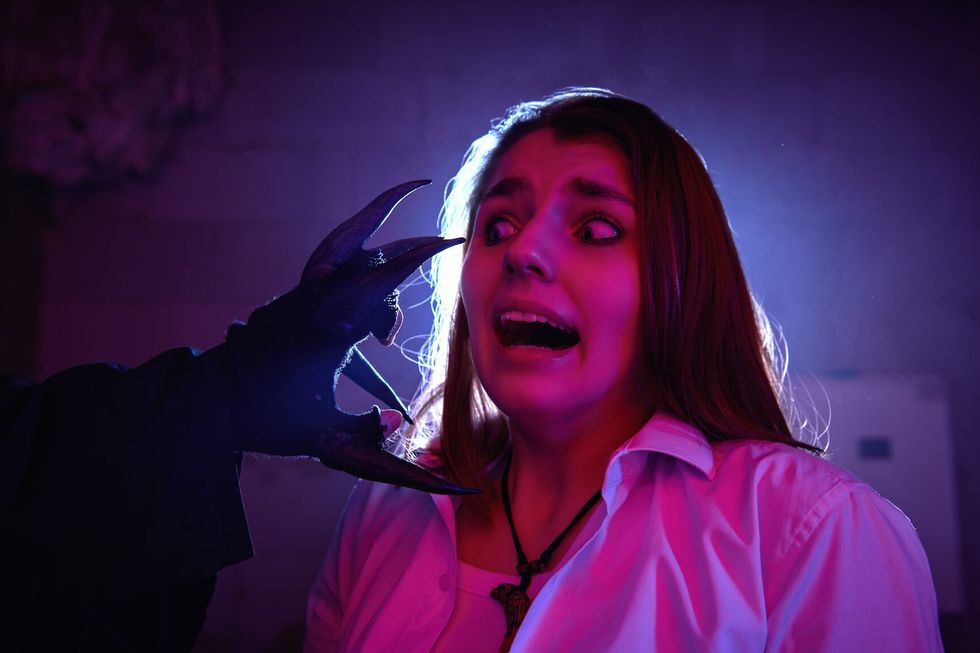 Haunted attraction A frightened girl screams in horror when she stumbles upon the hand of a monster with large black claws in a dark basement. Halloween quest.
