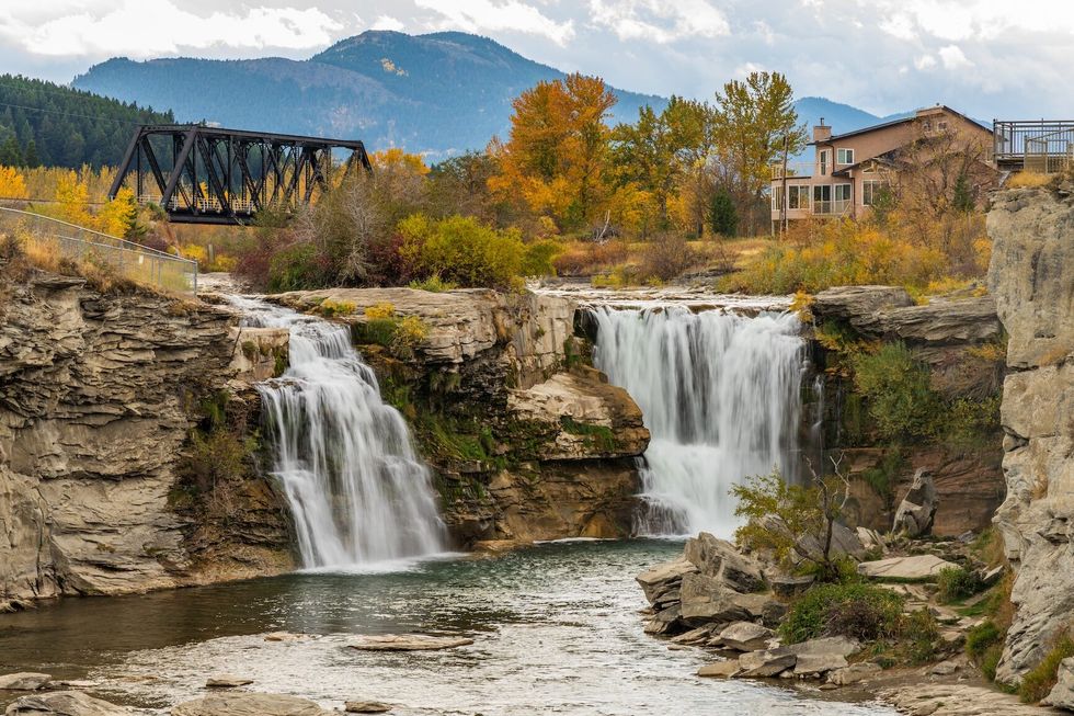 Lundbreck Falls, a waterfall of the Crowsnest River in autumn foliage season. An iron bridge for railroad tracks in the background. Alberta, Canada.