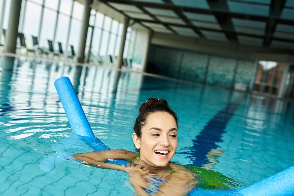 woman in swimsuit peacefully floats on a blue raft in an indoor spa swimming pool.