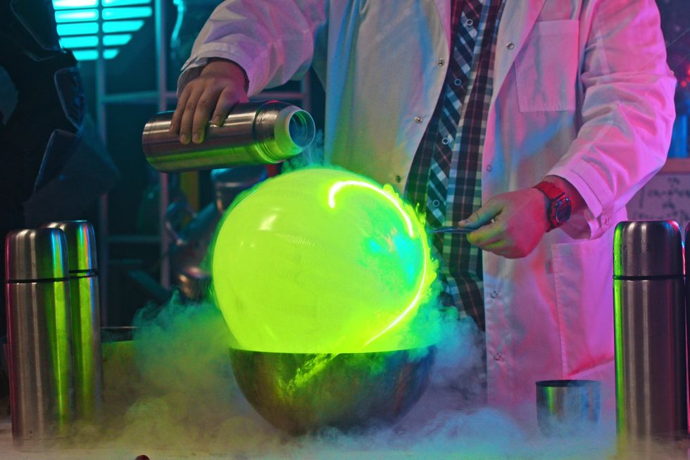 A man pours liquid nitrogen from a thermos on a green ballon