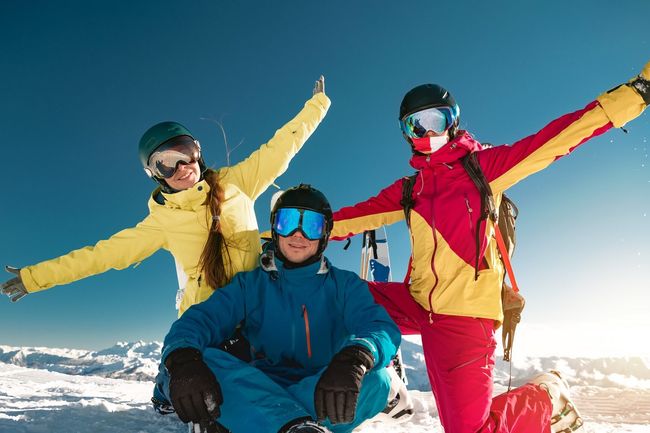 Three happy young skiers are sitting together. Ski resort winter weekend concept