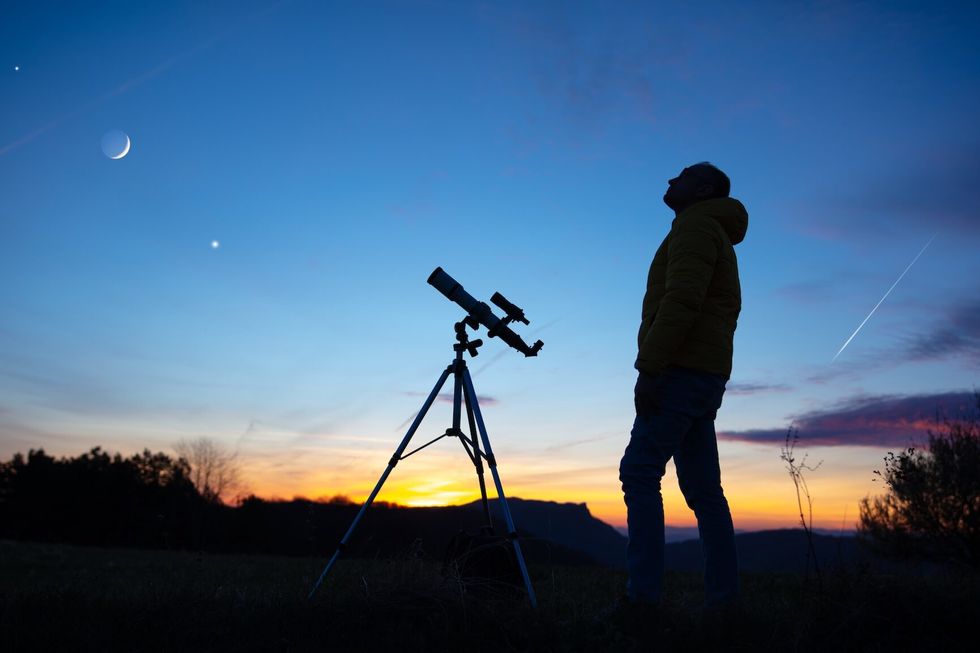 Amateur astronomer looking at the evening skies, observing planets, stars, Moon and other celestial objects with a telescope.